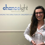 Picture of Clara Herrick standing in front of a wall with the chancelight logo on it. Clara is holding a plaque to recognize her winning.